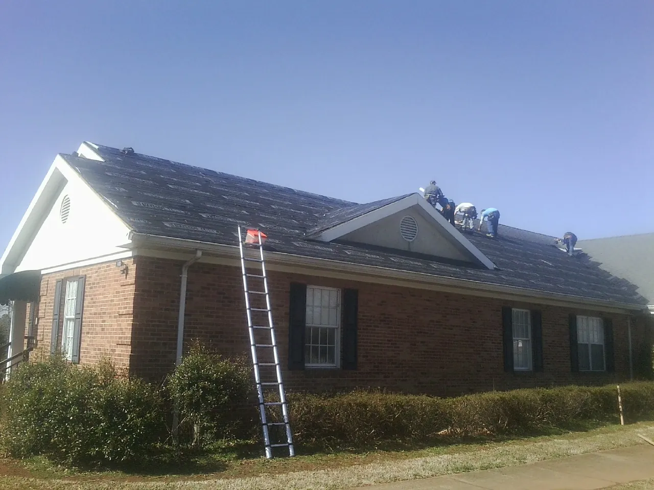 Crew tearing shingles off a brick ranch roof with a ladder set — Emergency Roof Repair work by our crew in Stayton