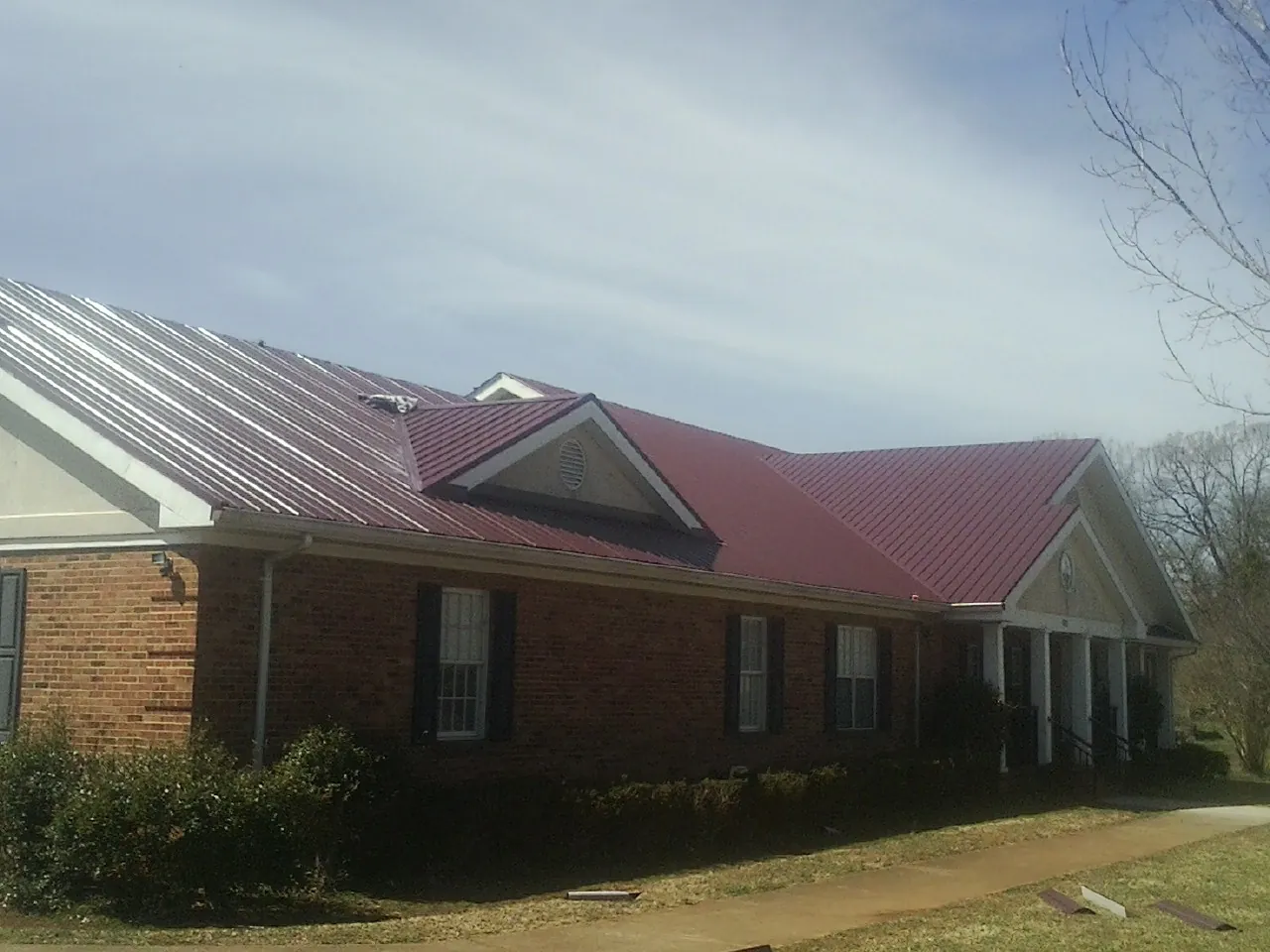 Red metal roof with gabled entries on a long brick building, from a Hail Damage Roof Repair job in Stayton