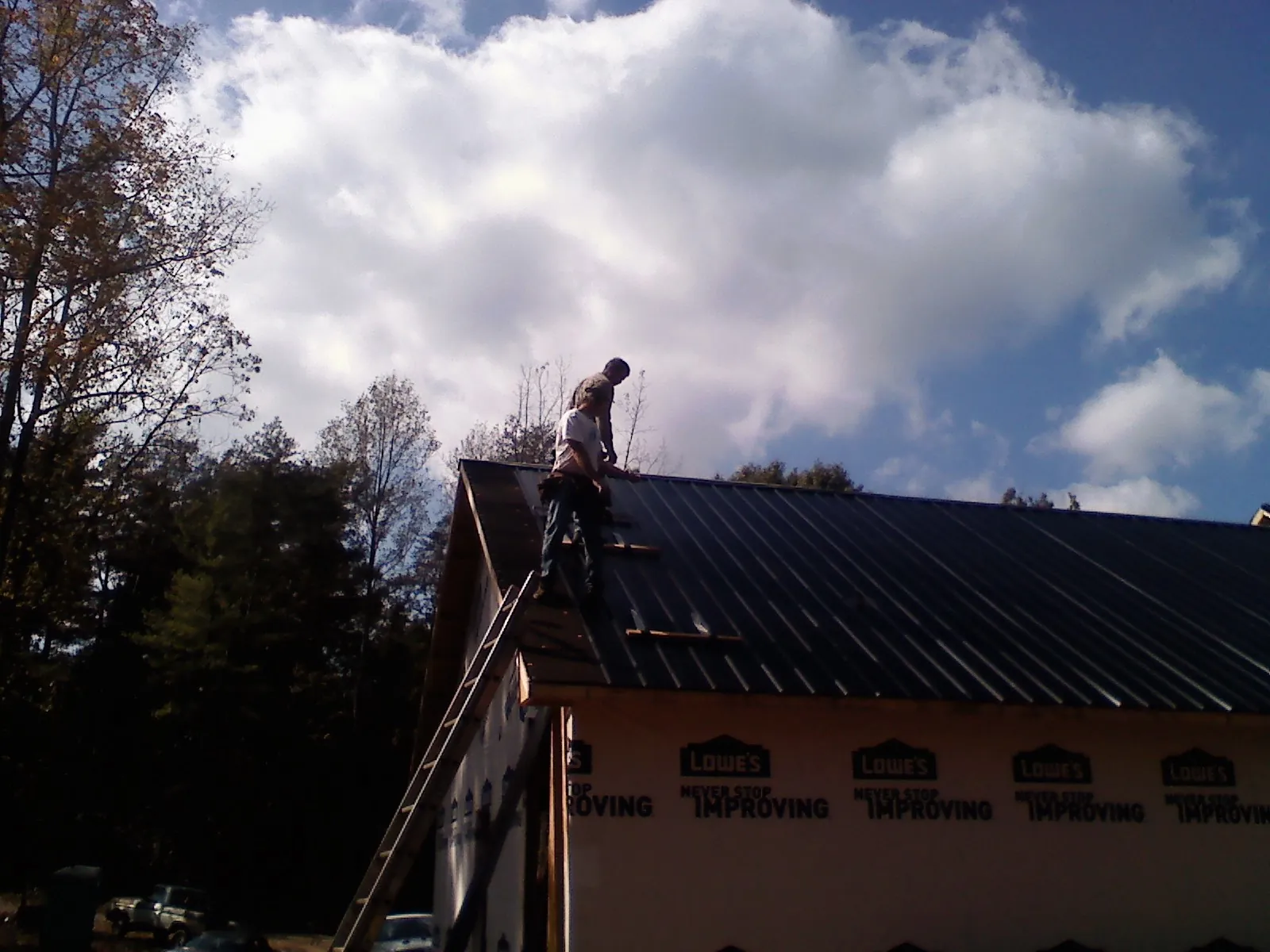 Roofer fastening dark metal panels high against a cloudy sky, from a Roof Inspection job in Stayton