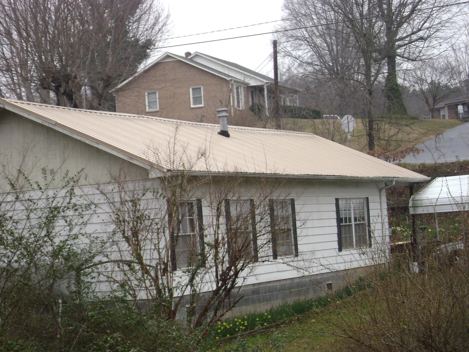 Tan metal roof on a white sided house set into a hillside — Commercial Roofing by Roofing Brothers in Stayton